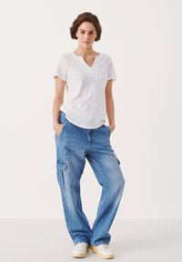 T-shirt bianco a maniche corte con scollo a V abbinato a pantaloni cargo in denim blu larghi, dotati di tasche laterali e vestibilità comoda.