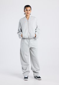 Ensemble sweat-shirt et pantalon de survêtement gris, fabriqué en tissu doux. La veste à fermeture éclair a une coupe décontractée, et le pantalon possède une taille ajustable.