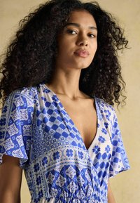 Blau gemustertes Kleid mit floralen und geometrischen Designs, kurzen Ärmeln, V-Ausschnitt und einem elastischen Bund für eine figurbetonte Passform.