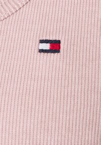 Tessuto lavorato a maglia rosa chiaro con una texture a coste, caratterizzato da un piccolo logo rettangolare ricamato in blu navy, rosso e bianco.