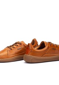 Zapatillas de cuero marrón con costuras tonales, diseño de cordones, cuello acolchado y suelas de goma. Presenta el logo de la marca en el costado.