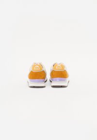 Baskets avec une tige en cuir beige et des accents orange. Présentent une semelle intermédiaire violette, des détails en daim texturé, et un logo circulaire sur le talon.