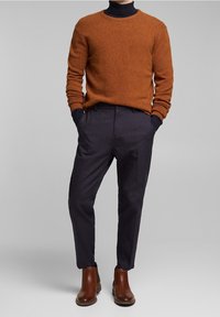 Sweter w odcieniu spalonej pomarańczy z mieszanki wełny, zestawiony z ciemnymi, dopasowanymi spodniami, brązowymi skórzanymi botkami za kostkę oraz widocznym granatowym golfem.