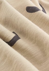 Beige strikket stof med mørkebrune abstrakte former. Teksturen er blød med synlige ribber, der skaber et subtilt bølge mønster.