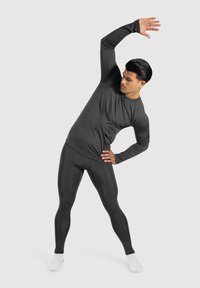 Donkergrijze sportieve longsleeve shirt en legging gemaakt van rekbaar, glad materiaal. Model is aan het stretchen met witte sokken.