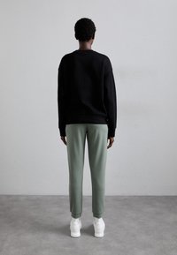 Svart sweatshirt med nedhasade axlar, ihop med ljusgröna tapered sweatpants och vita sneakers. Släta material och avslappnad passform.