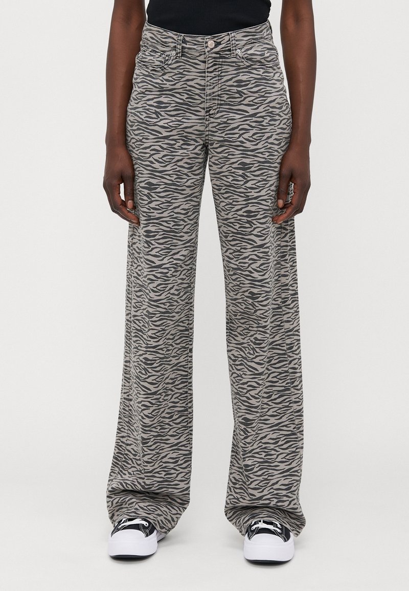 Jean à jambes larges avec un motif rayé zèbre gris et noir. Confectionné en denim doux, il présente une taille haute et une fermeture à bouton sur le devant.