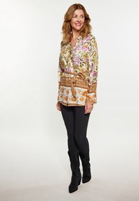 Blusa a fiori in crema con fiori viola, gialli e arancioni; vita cintata; abbinata a pantaloni skinny neri e stivali neri.