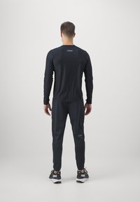 Tricou sportiv negru cu mânecă lungă și design ajustat, asociat cu pantaloni tapering asortați. Ambele au detalii discrecte cu logo. Material ușor.