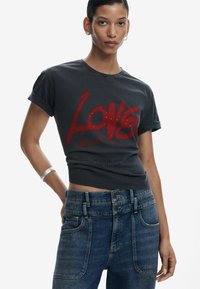 Graues Baumwoll-T-Shirt mit auffälligem roten "Love"-Grafik, hochgekrempelten Ärmeln, kombiniert mit hochgeschnittenen blauen Jeans aus Denim mit Fronttaschen und Knopfverschluss.