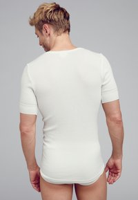 Weißes geripptes T-Shirt mit kurzen Ärmeln, das eine taillierte Form zeigt. Glatte Textur mit Rundhalsausschnitt, entworfen für eine enganliegende Passform.