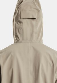 Beige waterdichte jas met een aangesloten capuchon, een soepele textuur en een detail met een achterzak. Naadloos ontwerp met minimale zichtbare stiksels.