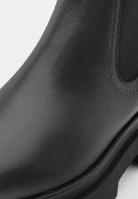 Svart Chelsea-støvel i lær med elastisk sidestykke og synlige sømmer på sålen, som viser en glatt tekstur og rund tå.