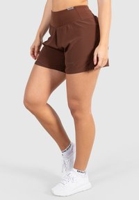 Bruna träningsshorts med en bred midja, lättviktig tyg och avslappnad passform. I kombination med vita träningsskor och strumpor med svarta detaljer.