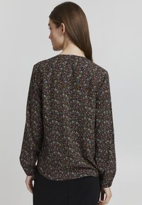 Svart bluse med blomster mønster i forskjellige farger, lange ermer, rund halsutskjæring og en avslappet passform, laget av lett, teksturert stoff.
