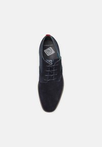 Scarpa in suede blu navy con superficie testurizzata e dettagli perforati. Presenta un design con lacci e un accento rosso a contrasto sul tallone.