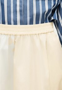 Μπλε πουκάμισο με λευκές κάθετες ρίγες, μπουδωμένο σε μια κρεμ φούστα με ψηλή μέση και ελαστική ζώνη με πιέτες.