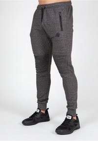 Slim-fit, mørkegrå joggers med ribbede detaljer langs benene, lynlåslomme og elastisk talje; parret med sorte træningssko.