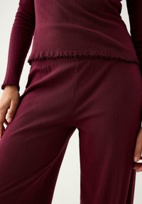 Burgundyribbat stickad topp och matchande byxor har volangkant, elastisk passform och mjuk textur, vilket ger en koordinerad loungeklädsel.
