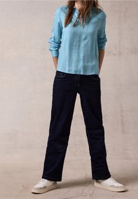 Blusa azzurra chiara a maniche lunghe con motivo geometrico; abbinata a jeans blu scuro; sneakers bianche con dettagli testurizzati.