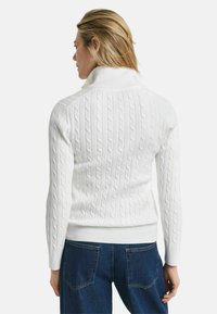 Weißer Kabelstrickpullover mit hohem Kragen, geripptem Saum und Bündchen, von hinten betrachtet. Texturiertes Muster über den gesamten Körper.