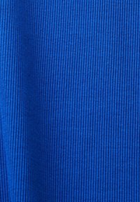 Gros plan d'un tissu tricoté côtelé bleu montrant des lignes texturées verticales et de légers plis dans le tissu.