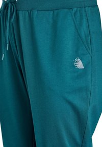 Sinised riidest püksid elastse vöökohaga, paelaga, küljetaskuga ja väike valge logo tasku lähedal. Pehme tekstuur.