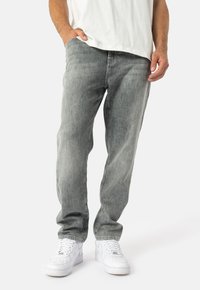 Gaiši pelēki džinsi ar brīvu piegriezumu, kam ir smalki, izbalējuši tekstūras. Apvienoti ar baltiem kedām kontrasta radīšanai.