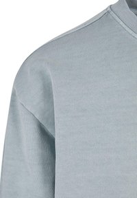 Světle modrá mikina s texturovaným pletením, s kulatým výstřihem a spadlými rameny, zobrazená od ramen v úžasu.