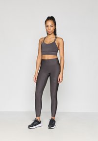 Sutiã desportivo cinza-escuro e leggings de cintura alta feitos de material liso e elástico, complementados por sapatilhas pretas.