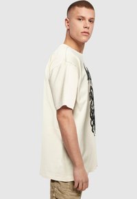 Bomulds T-shirt i off-white med et sort grafisk design. Løs pasform med korte ærmer og rund halsudskæring.