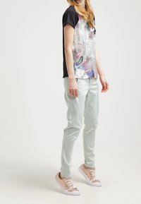 Květinové grafické tričko s černými rukávy, mátově zelené kalhoty a růžově zlaté tenisky se šněrováním. Oblečení má volný střih a pohodový styl.