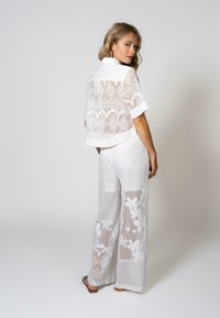 Ensemble deux pièces en dentelle blanche comprenant un haut à manches courtes avec un col et un pantalon à jambes larges orné de motifs floraux et géométriques.