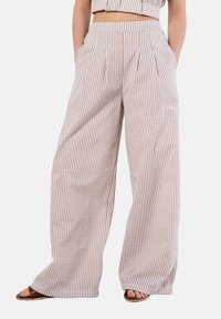Pantalons larges en tissu léger avec des rayures verticales beiges et blanches, dotés de plis profonds sur le devant et de poches latérales.