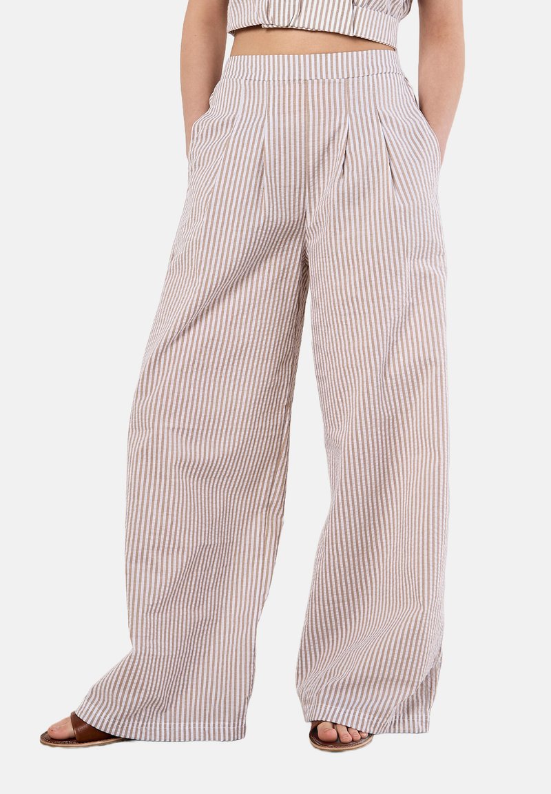 Pantalons larges en tissu léger avec des rayures verticales beiges et blanches, dotés de plis profonds sur le devant et de poches latérales.