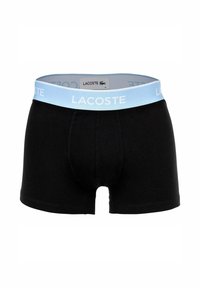 Boxer neri in cotone con una cintura elastica azzurro chiaro che presenta il logo "LACOSTE" in bianco. Lunghezza fino a metà coscia con una vestibilità aderente.