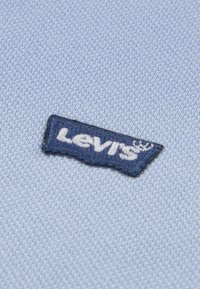 Tissu texturé bleu clair avec un patch logo Levi's bleu marine, présentant un texte blanc brodé sur le bord du patch.