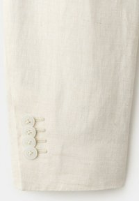 Mouw van een crème linnen jas met vier bijpassende crèmekleurige knopen in een verticale rij vlakbij de manchet genaaid.