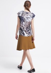 Top con motivo floreale in tonalità di blu e beige, abbinato a una gonna senape di lunghezza al ginocchio. L'outfit presenta maniche a sbuffo e una silhouette svasata.
