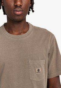 Oliwkowa bawełniana koszulka z krótkim rękawem, okrągłym dekoltem i kieszonką na lewej piersi z naszywką z logo marki. Gładka struktura.