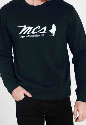 Schwarzes Langarmshirt mit weißem Schriftzug "MCS Rugged and Refined Since 1987" und einer Silhouette einer Person mit Mantel und Hut auf der Brust.