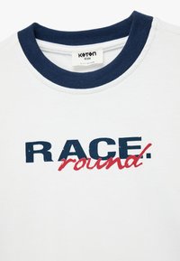 Hvid bomulds t-shirt med en marineblå rund halsudskæring og grafisk tekst i marineblå og rød, der står "RACE. round."