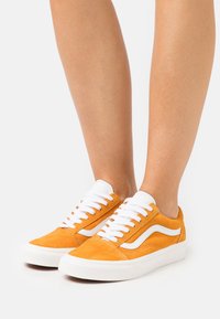 Baskets en daim orange avec lacets blancs et accents latéraux. Bout arrondi, semelle blanche plate, et design classique avec des détails de couture prononcés.