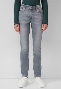 Jean en denim gris slim fit avec un lavage délavé, un léger effet de frottement, cinq poches et une fermeture éclair. Associé à des baskets blanches.