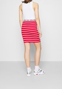 Rot-weiße gestreifte Bodycon-Rock mit einem schwarzen Markengummi, kombiniert mit weißen und silbernen Sportschuhen und weißen Knöchelsocken.