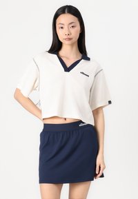 Vit kort topp med marin krage och logotyp, kombinerad med en marin skort. Tyget verkar vara texturerat; avslappnad passform och korta ärmar.