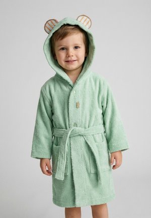 Young child wearing a light green hooded bathrobe with bear ears, tied at the waist, smiling at the camera against a plain background.