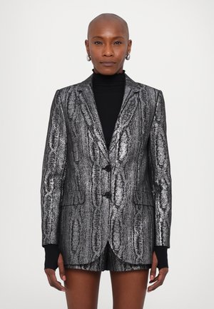Metallic black blazer with textured silver pattern, single-button closure, and front pockets. Worn over a black turtleneck.
