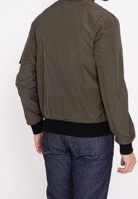 Olivgrön bomberjacka med en slät yta, ribbade svarta cuffs och midja. Har en avslappnad design och är matchad med mörk denimjeans.