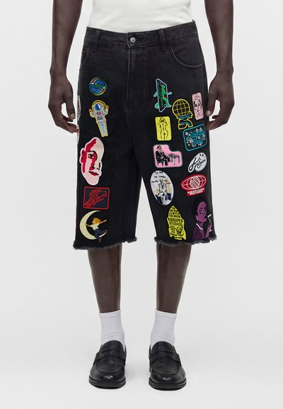 Black knee-length denim shorts with colorful eclectic patches worn with white socks and black shoes.